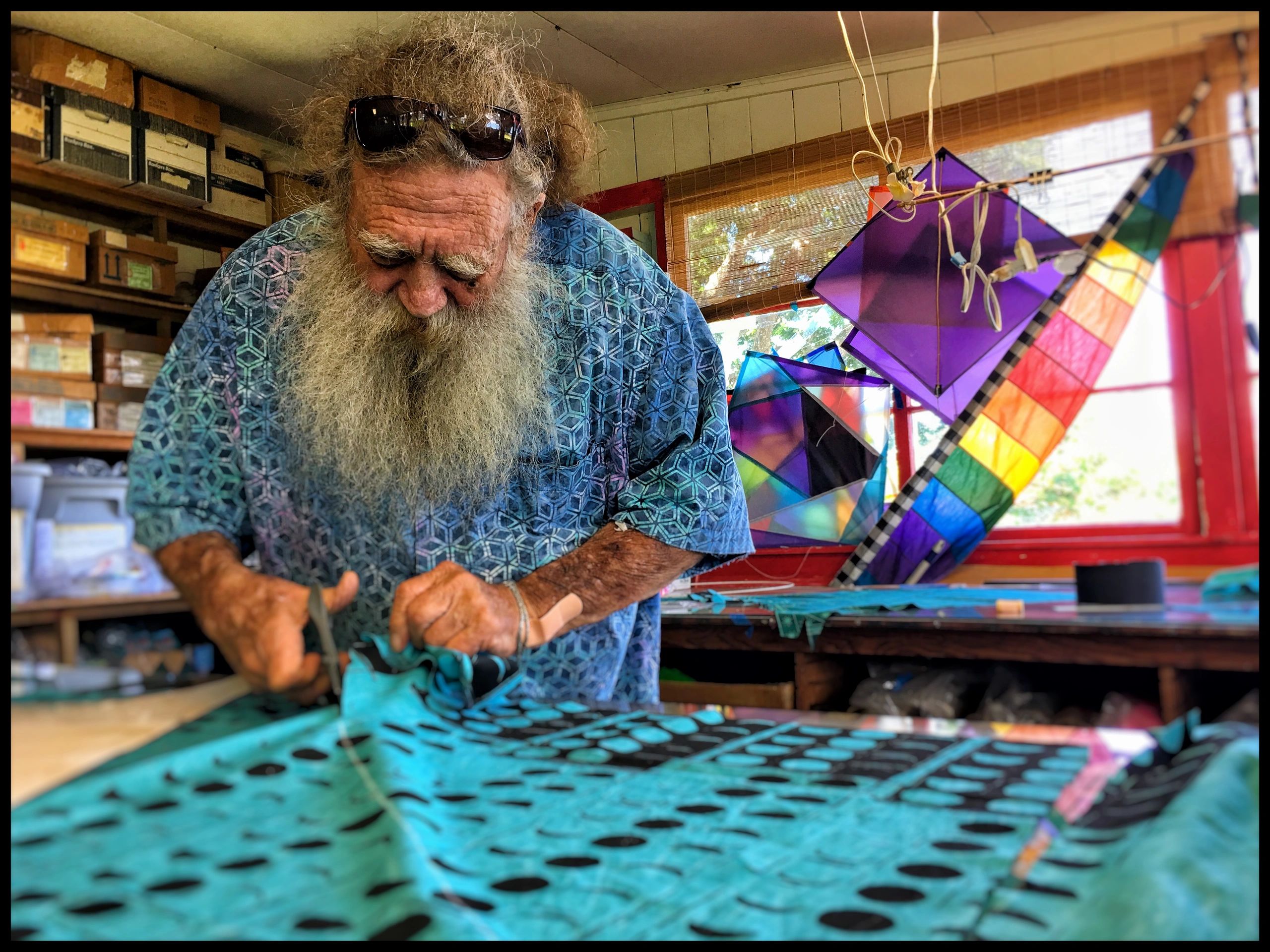 Kite maker cutting material inside the colorful Big Wind Kite Factory workshop in Maunaloa