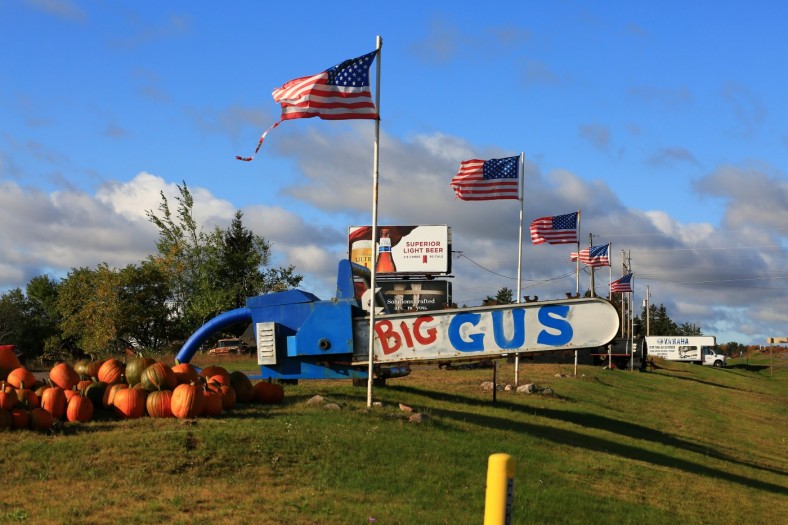 Giant blue chainsaw named Big Gus at Da Yoopers Tourist Trap in Ishpeming with roadside flags and signs behind it