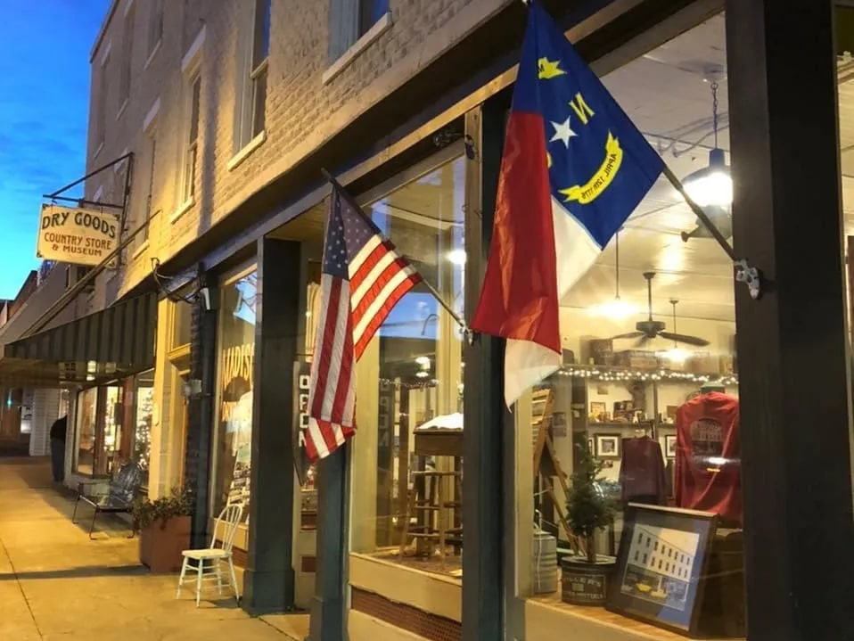 Madison Dry Goods storefront with flags, display windows and a hanging Country Store and Museum sign
