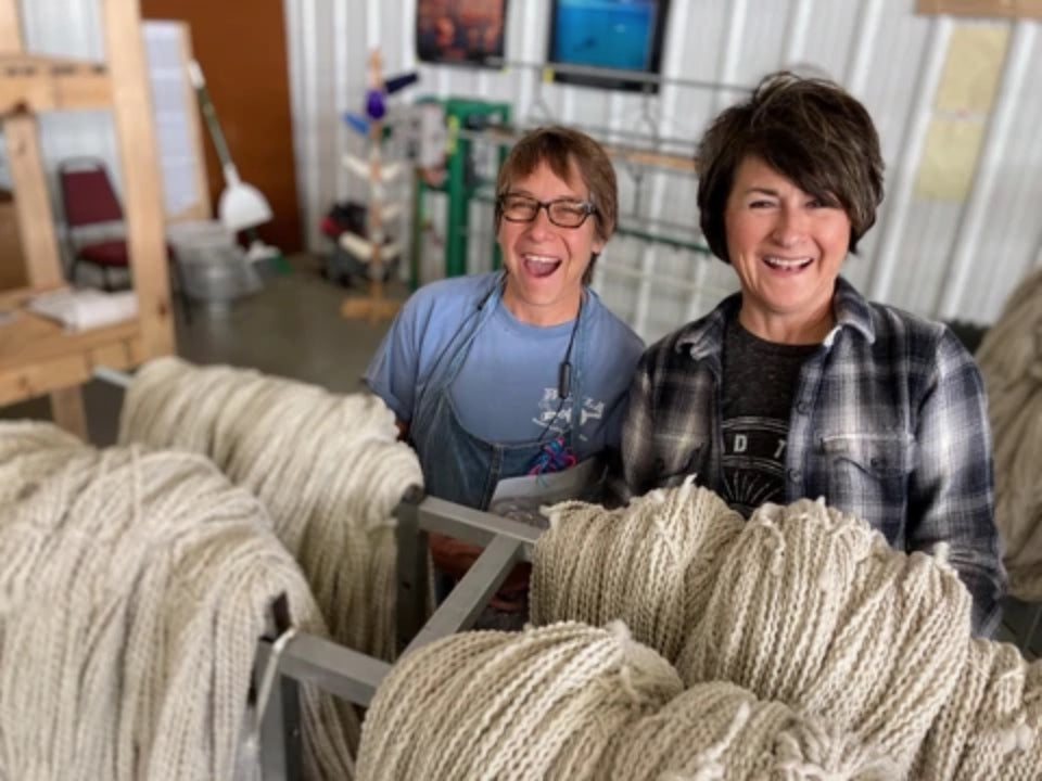 Two people beside rows of wool yarn inside Mountain Meadow Wool Mill in Buffalo