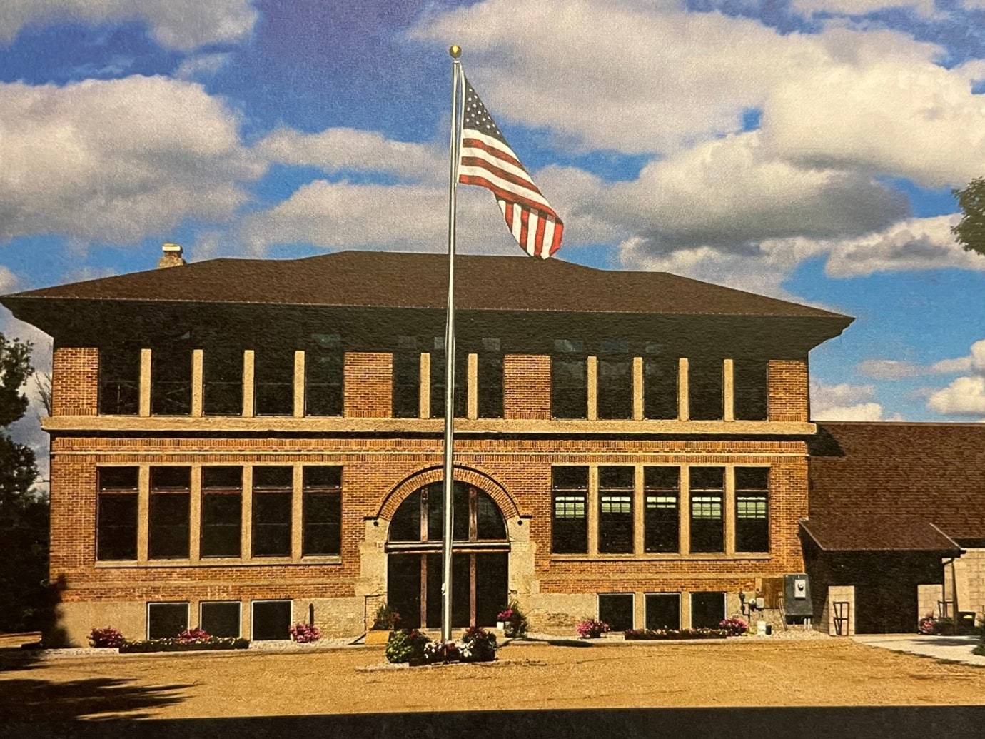 Restored brick Nome Schoolhouse beneath an American flag and broad prairie sky