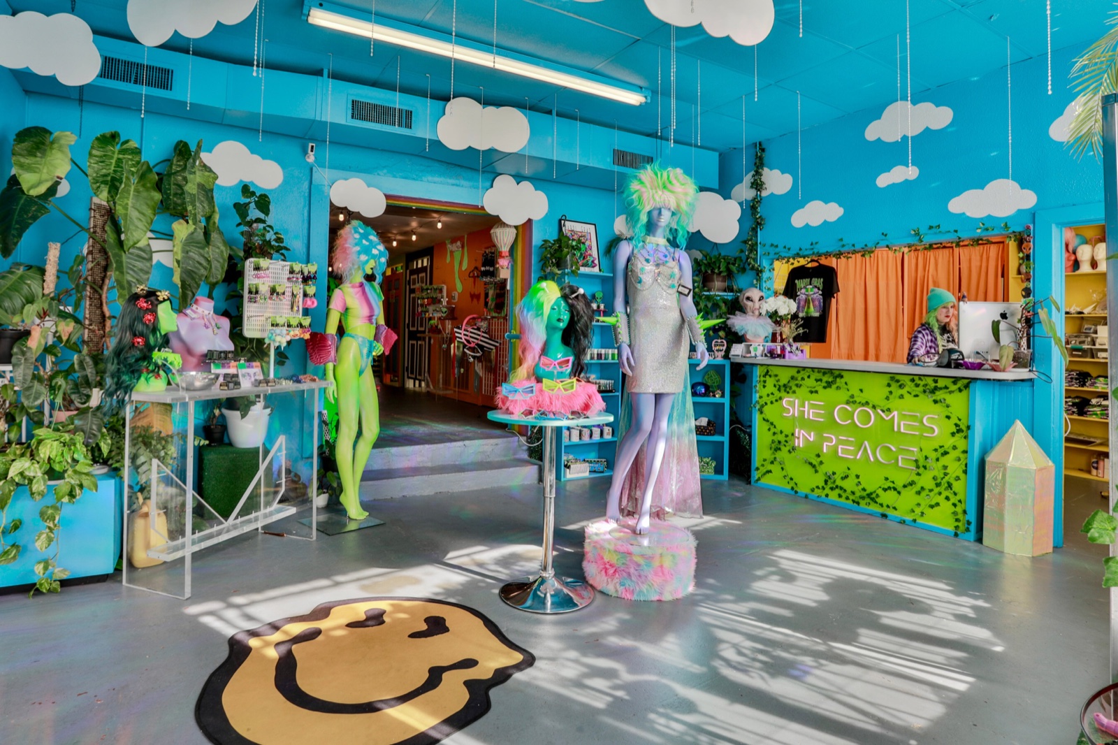 Wide turquoise interior of She Comes in Peace with cloud decorations, colorful wigs, mannequins and the costume-shop counter
