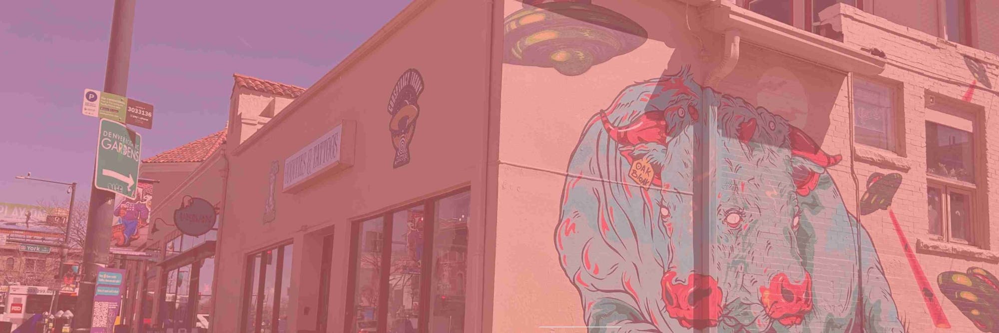 Wide street-level view of The Learned Lemur's colorful Colfax storefront and mural