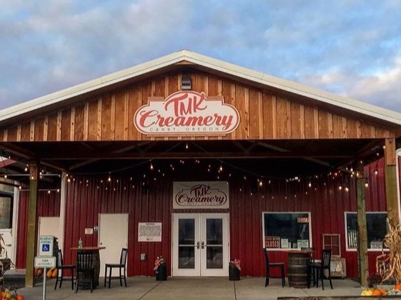 Red farm building with TMK Creamery signs above the covered visitor entrance in Canby