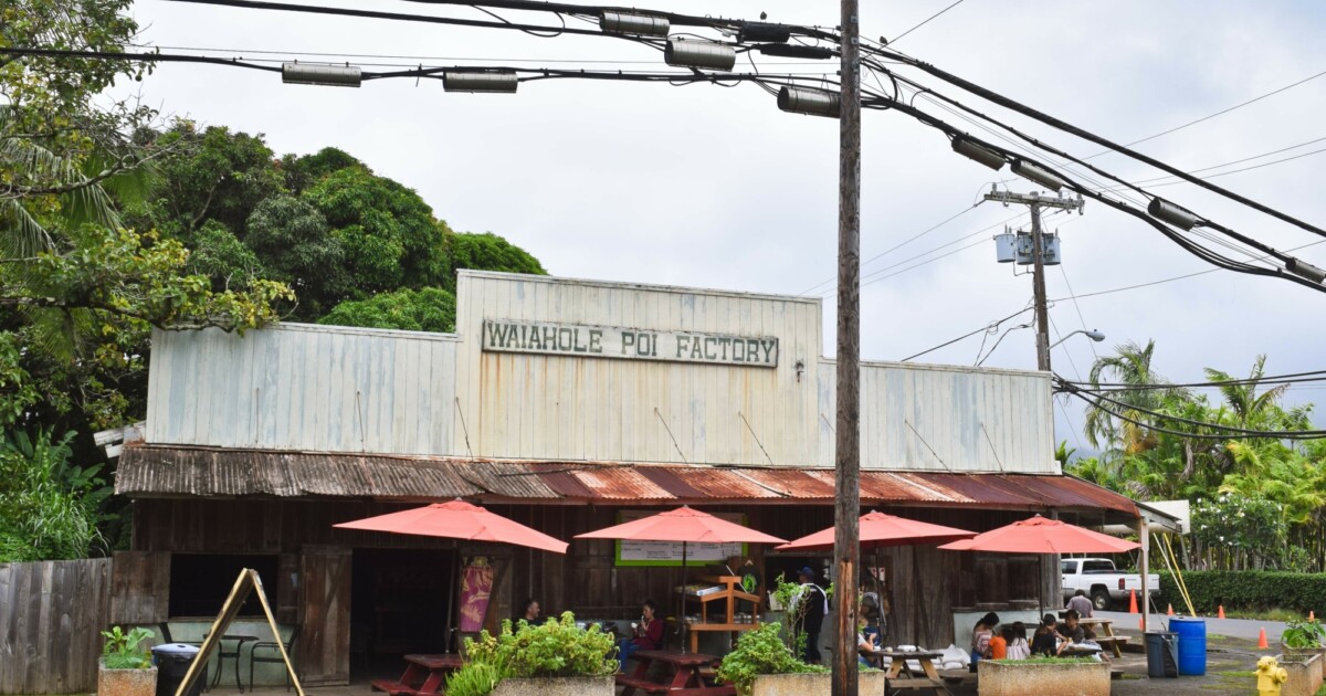 Historic Waiāhole Poi Factory exterior at the 48-140 Kamehameha Highway valley property with its sign and red outdoor umbrellas