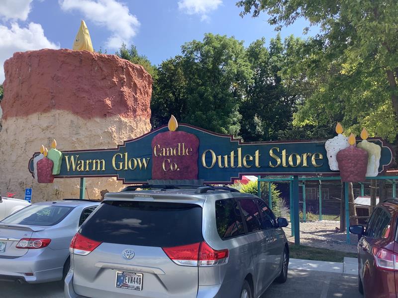 Warm Glow Candle Outlet entrance sign in front of the giant candle sculpture in Centerville